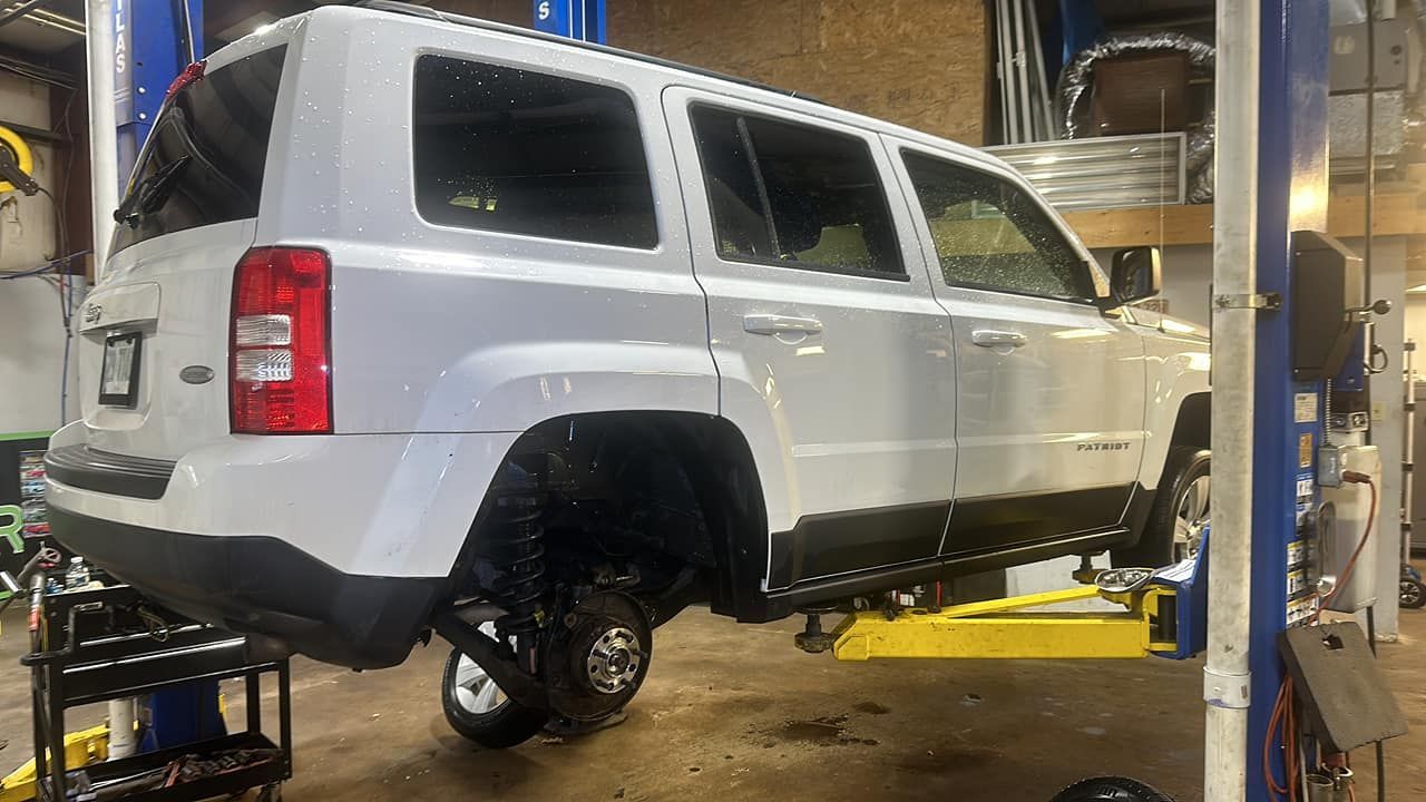 A white jeep patriot is parked on a lift in a garage.