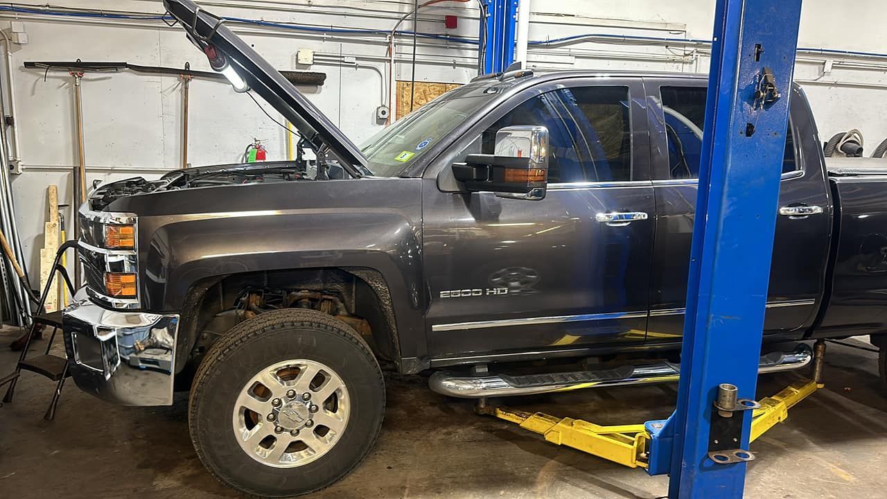 A truck with its hood up is on a lift in a garage.