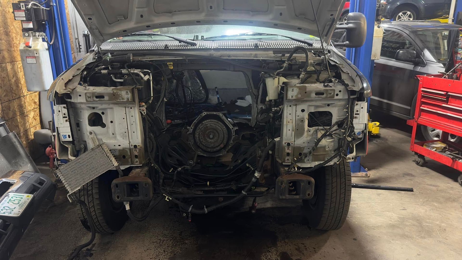 A car with the hood up is being worked on in a garage.