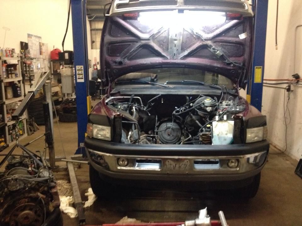 A truck with the hood up is on a lift in a garage.
