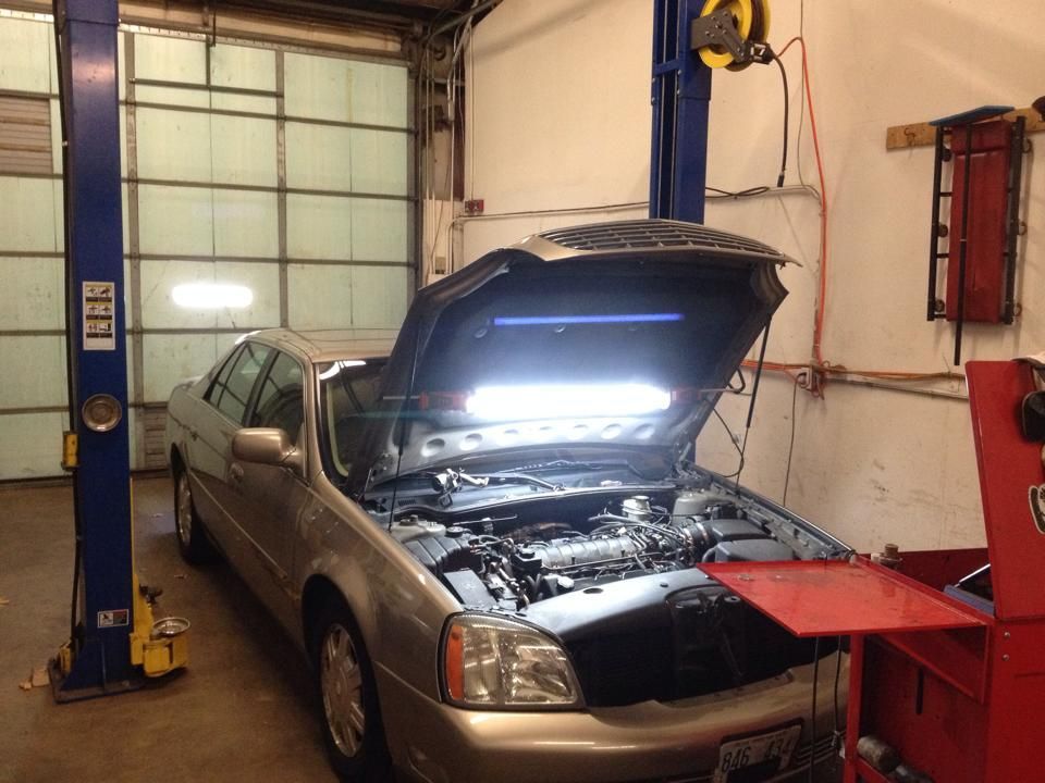 A car with the hood open is on a lift in a garage