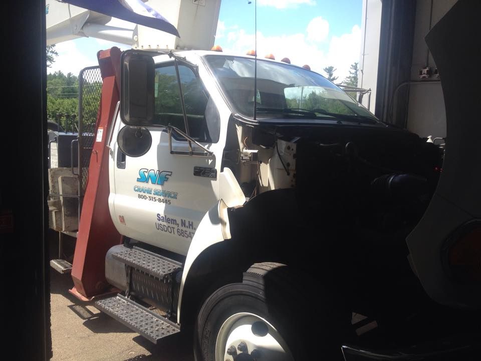 A white tow truck with the hood up is parked in a garage.