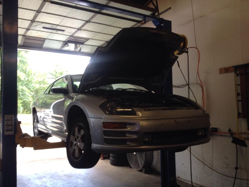 A silver car with the hood up is on a lift in a garage
