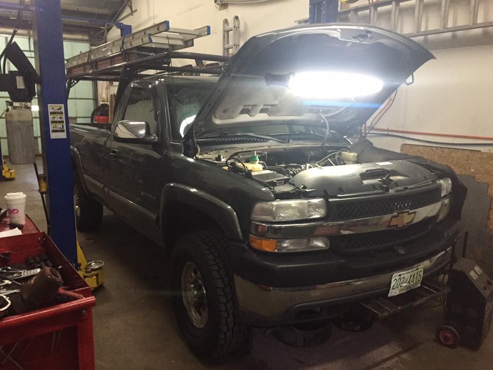 A truck with the hood up is sitting on a lift in a garage.