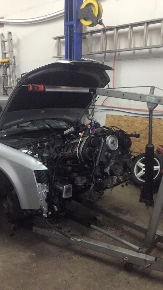 A car is being worked on in a garage with the hood open.