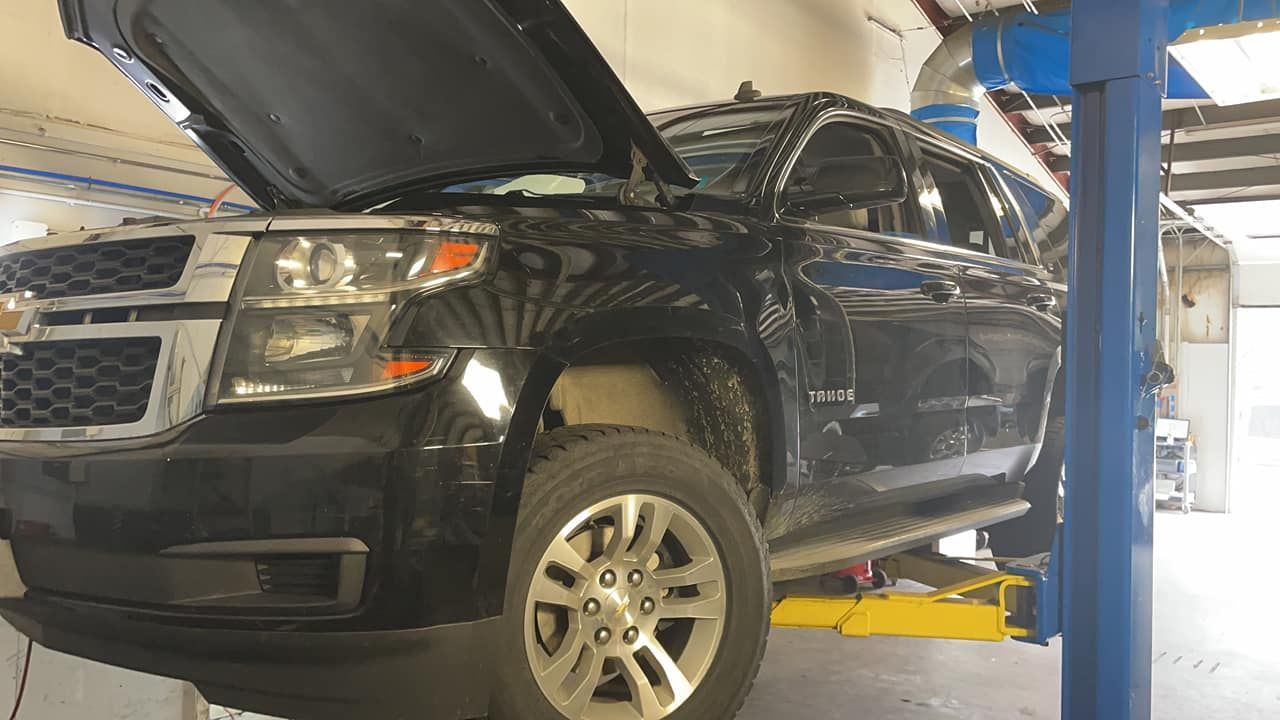 A black suv with the hood up is on a lift in a garage.