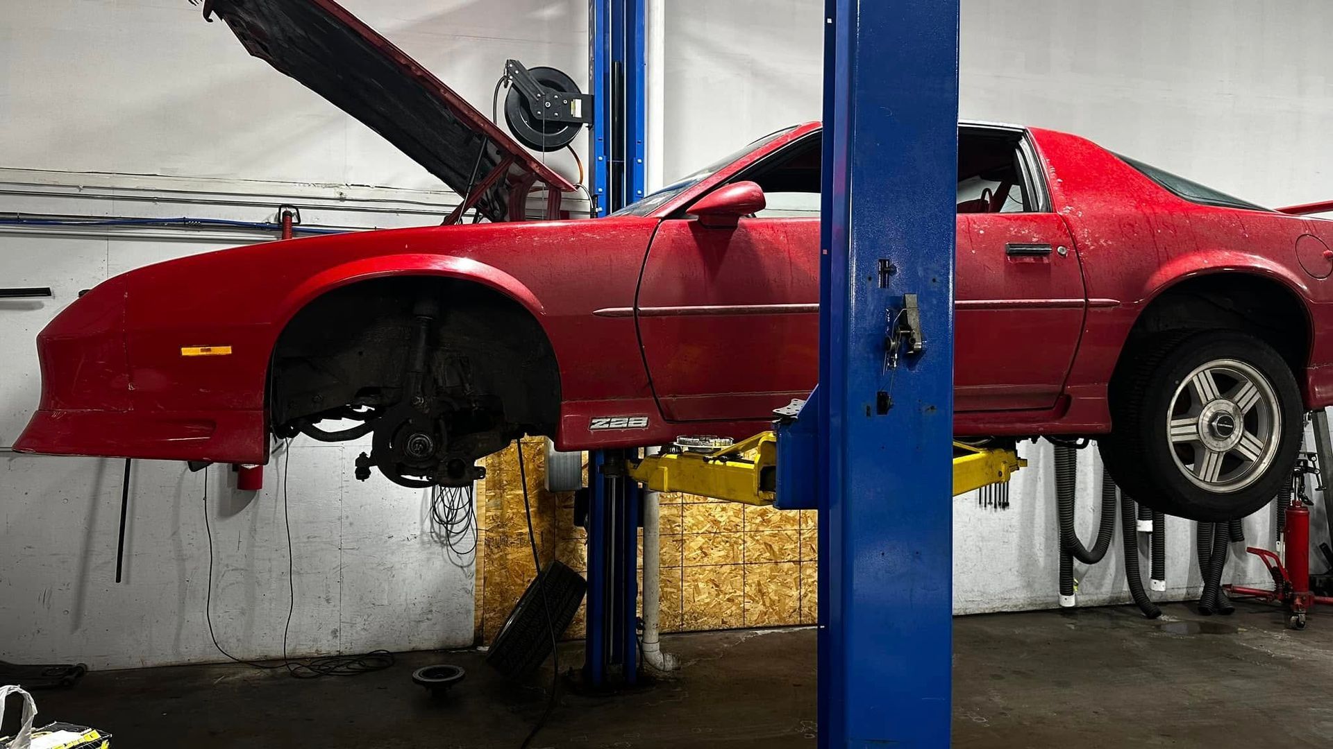 A red car is on a lift in a garage.