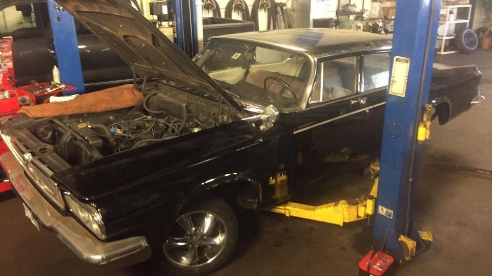 A black car with the hood up is on a lift in a garage.