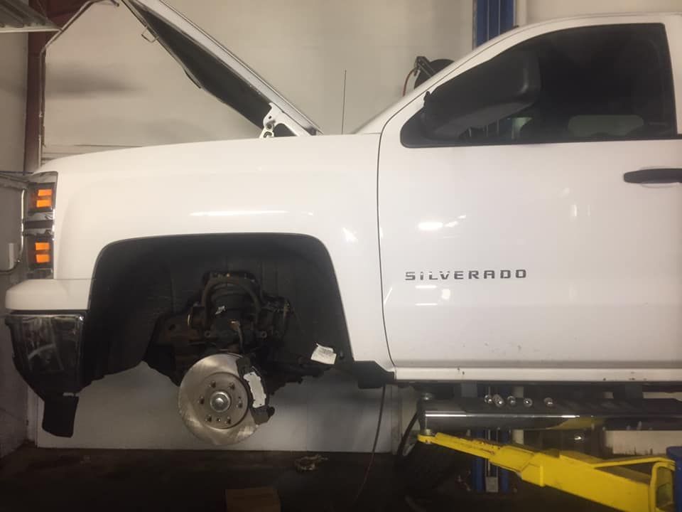 A white silverado truck is sitting on a lift in a garage.