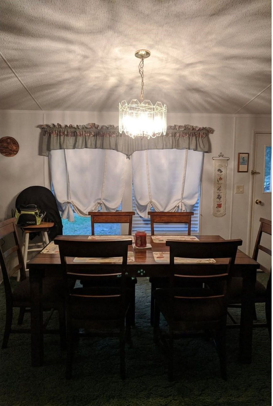 Dining room with chandelier, wooden table and chairs, and curtained windows at night.