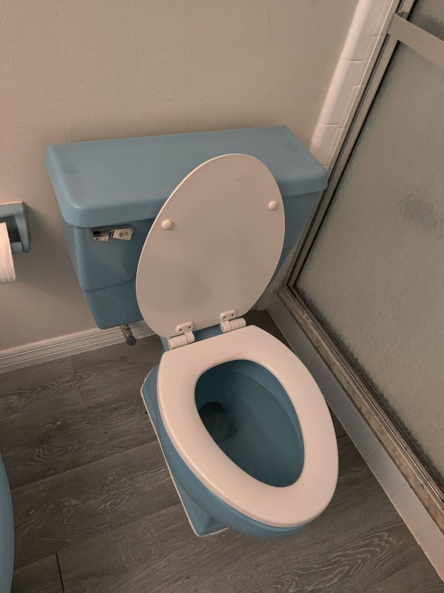Open toilet with blue tank and seat in a small bathroom next to a shower door.
