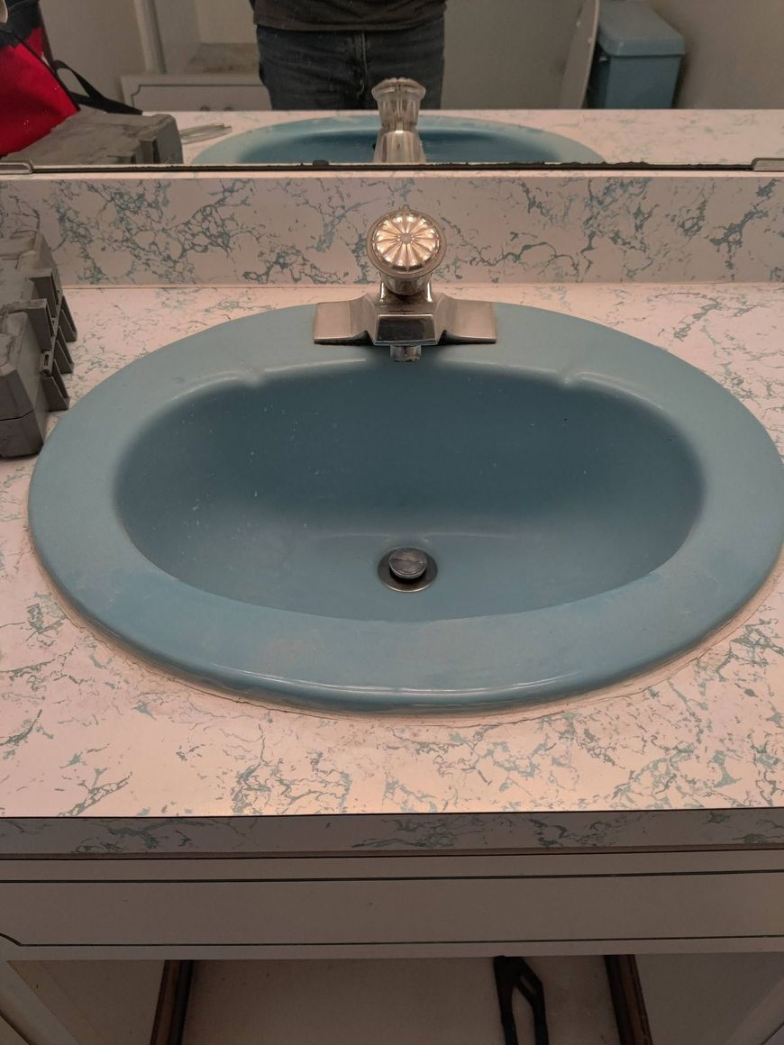 Blue bathroom sink with mirror and marble-pattern countertop, showing a faucet and drain.