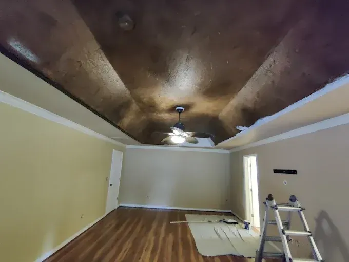 Empty living room with wood floor, beige walls, dark textured ceiling, and a ladder near the right wall.