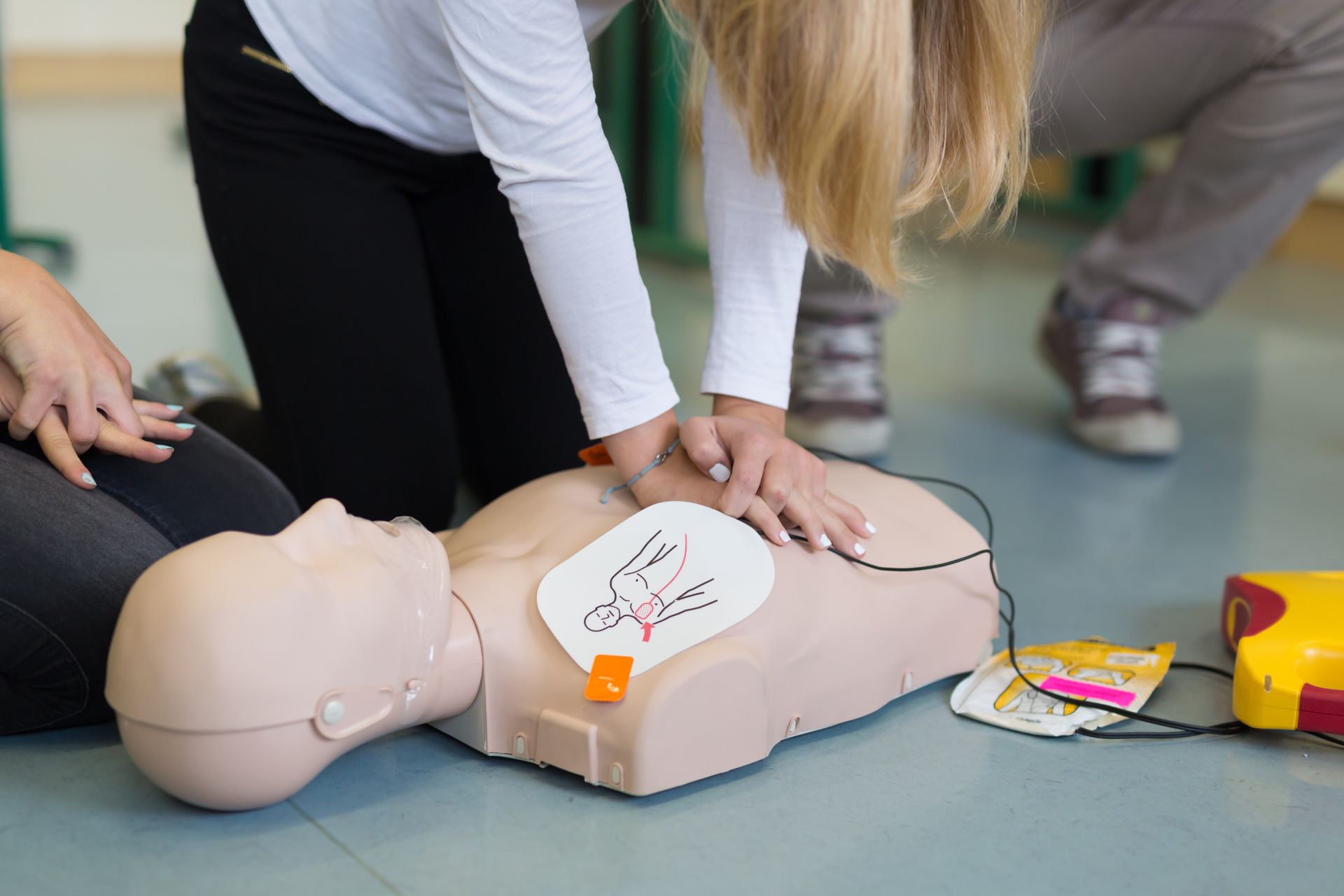 People practicing CPR on a training mannequin with AED pads and rescue tools nearby