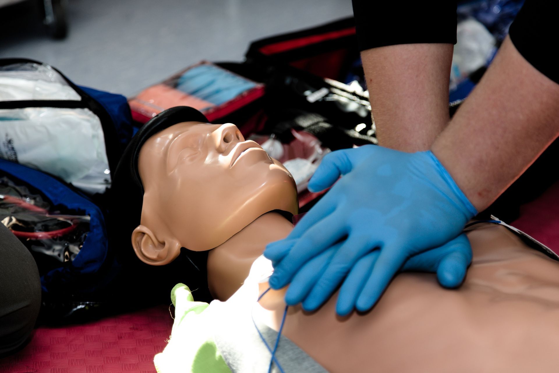 CPR training mannequin on the floor with blue-gloved hands performing chest compressions
