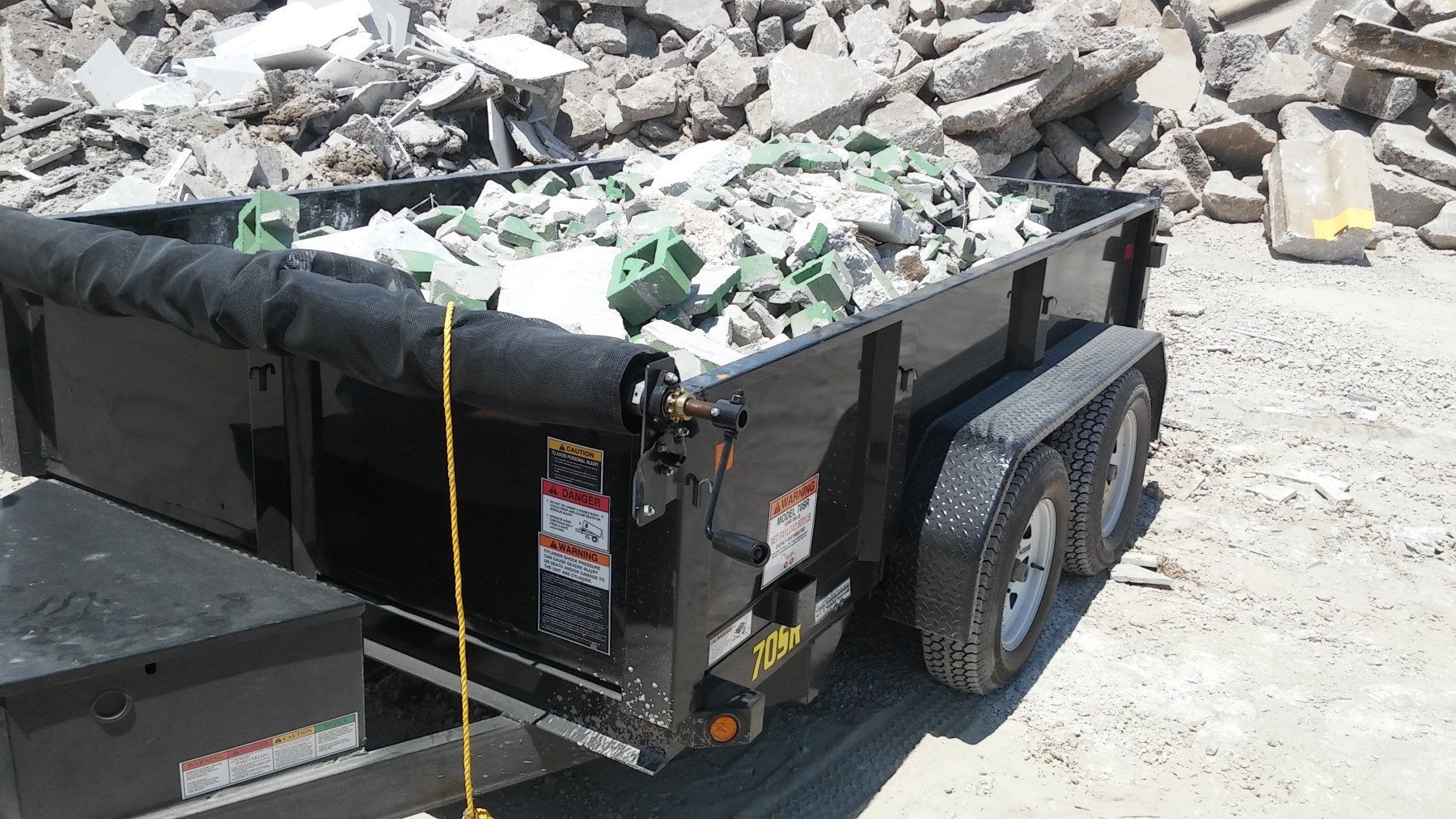 Black trailer filled with construction debris on a sunny day.