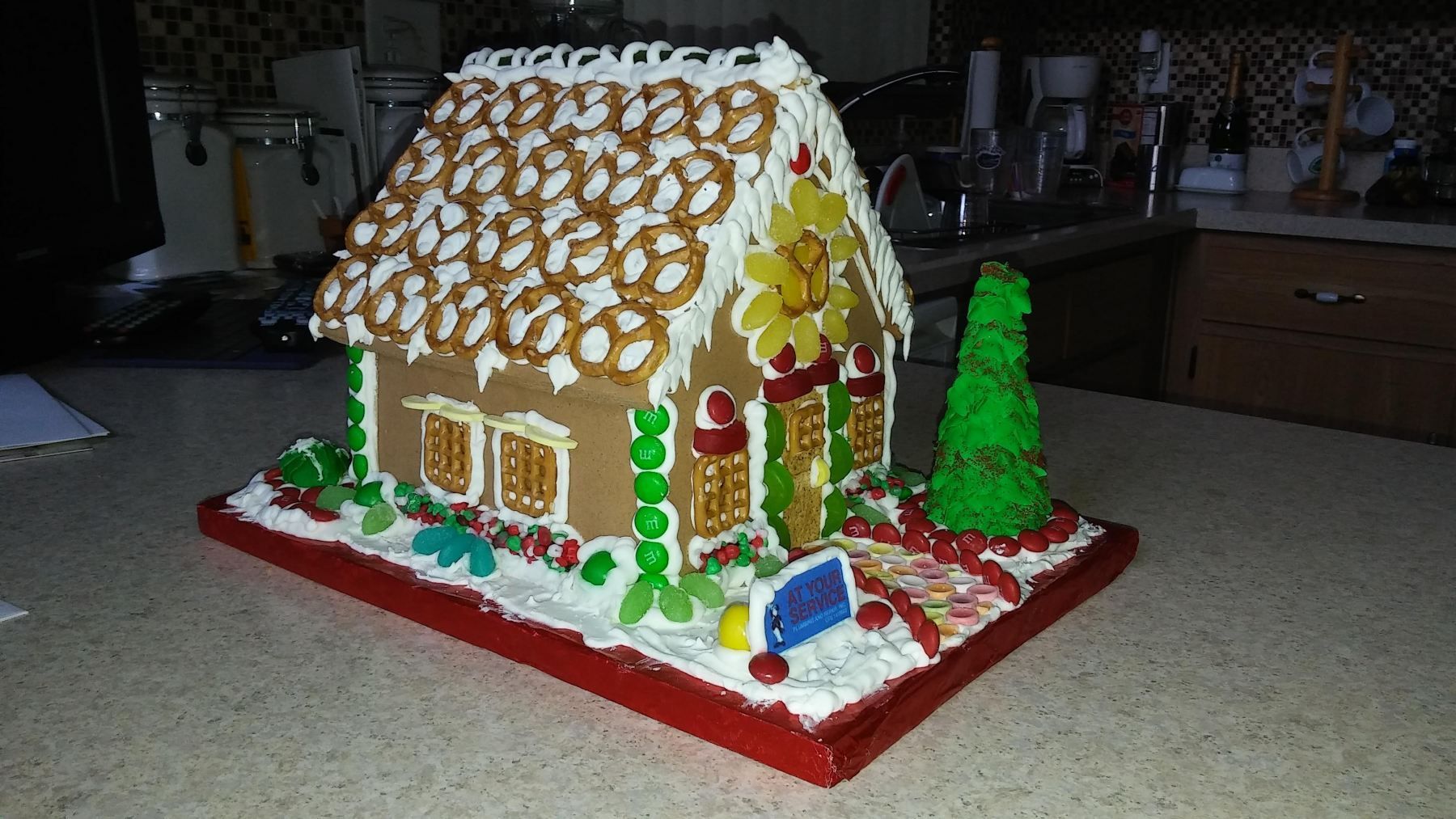 Gingerbread house decorated with pretzels, candy, and icing, set on a red base.