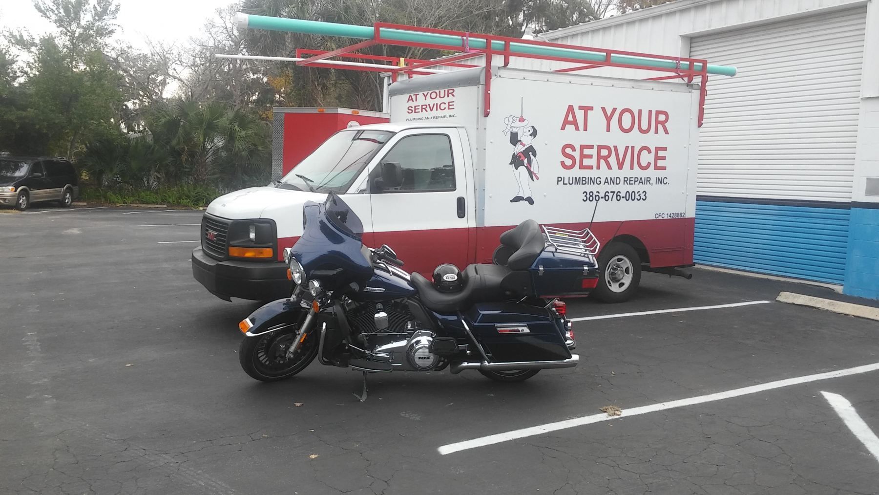 A red and white service truck parked next to a black motorcycle; pipes on top.