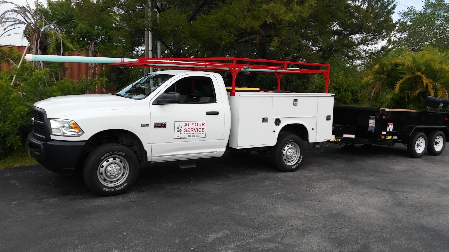White work truck with red rack, towing a trailer on a paved surface.