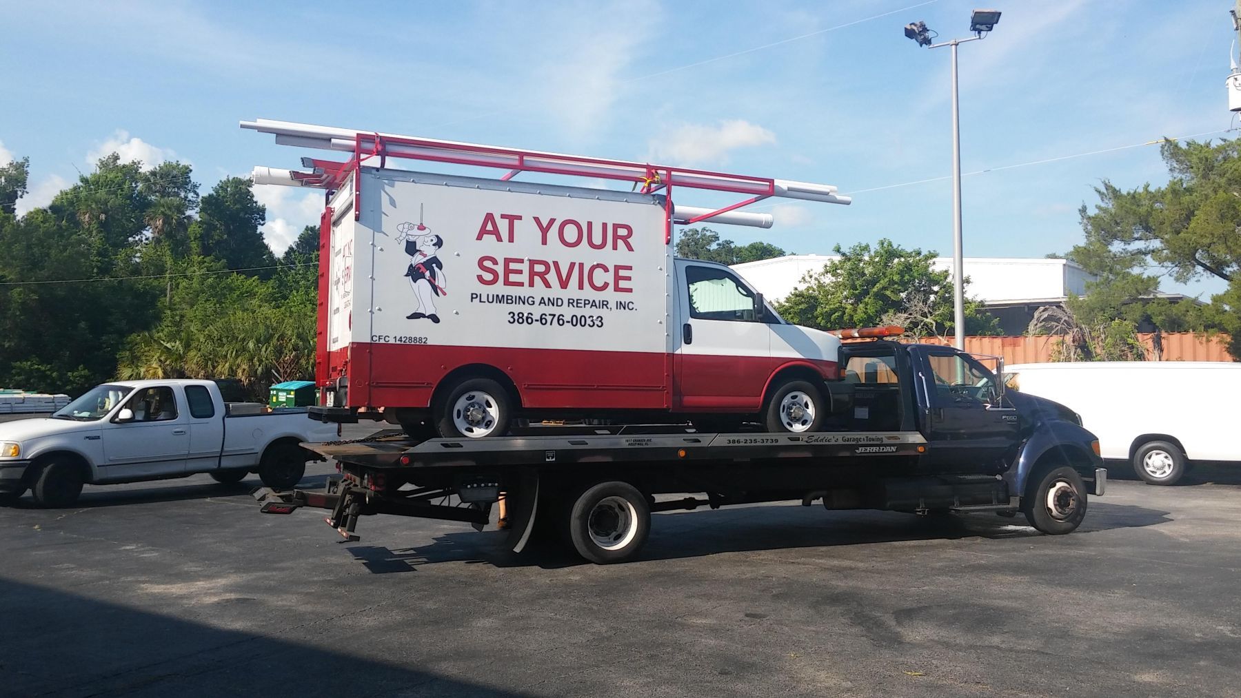 A work van on a flatbed tow truck. The van is white and red, with a ladder on top.