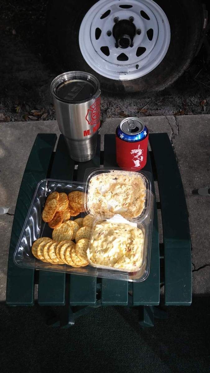 Snack tray with fried food, crackers, coffee, and a 7-Up can on a small green table near a tire.