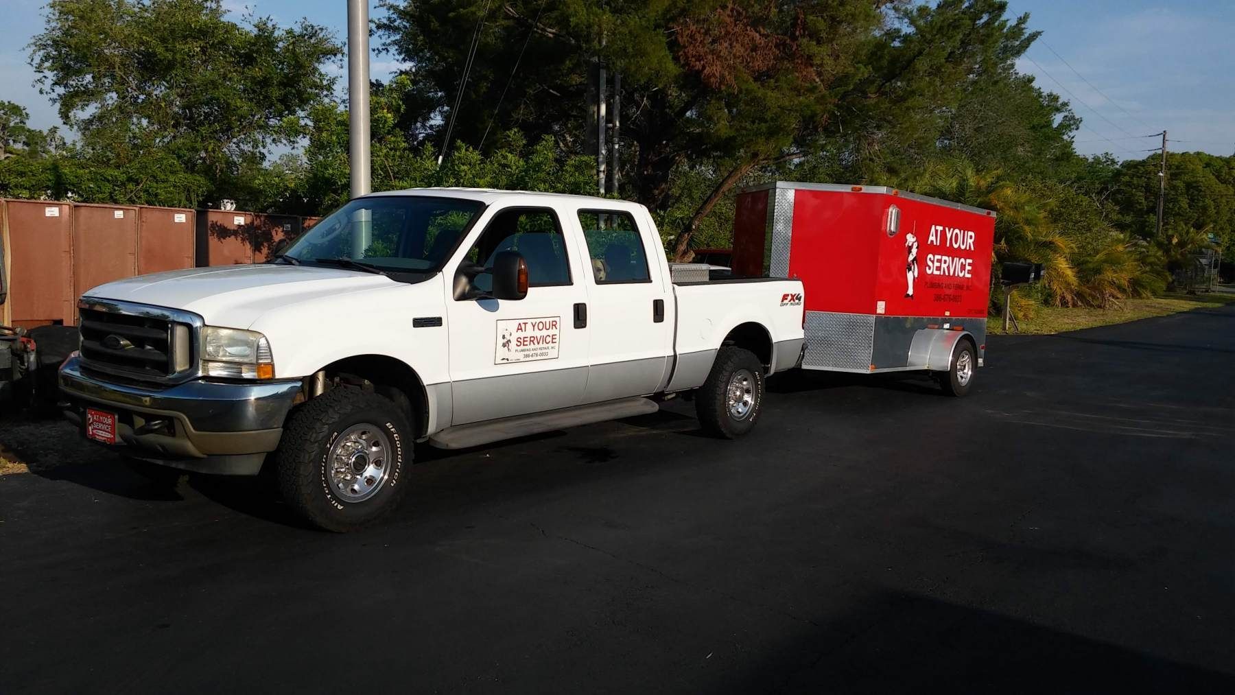 White pickup truck towing a red trailer with text on the side, parked on asphalt.