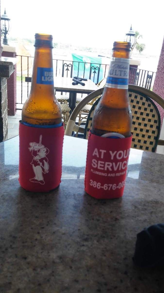 Two beer bottles in red koozies on a table outside. One koozie has a cartoon pig, the other says