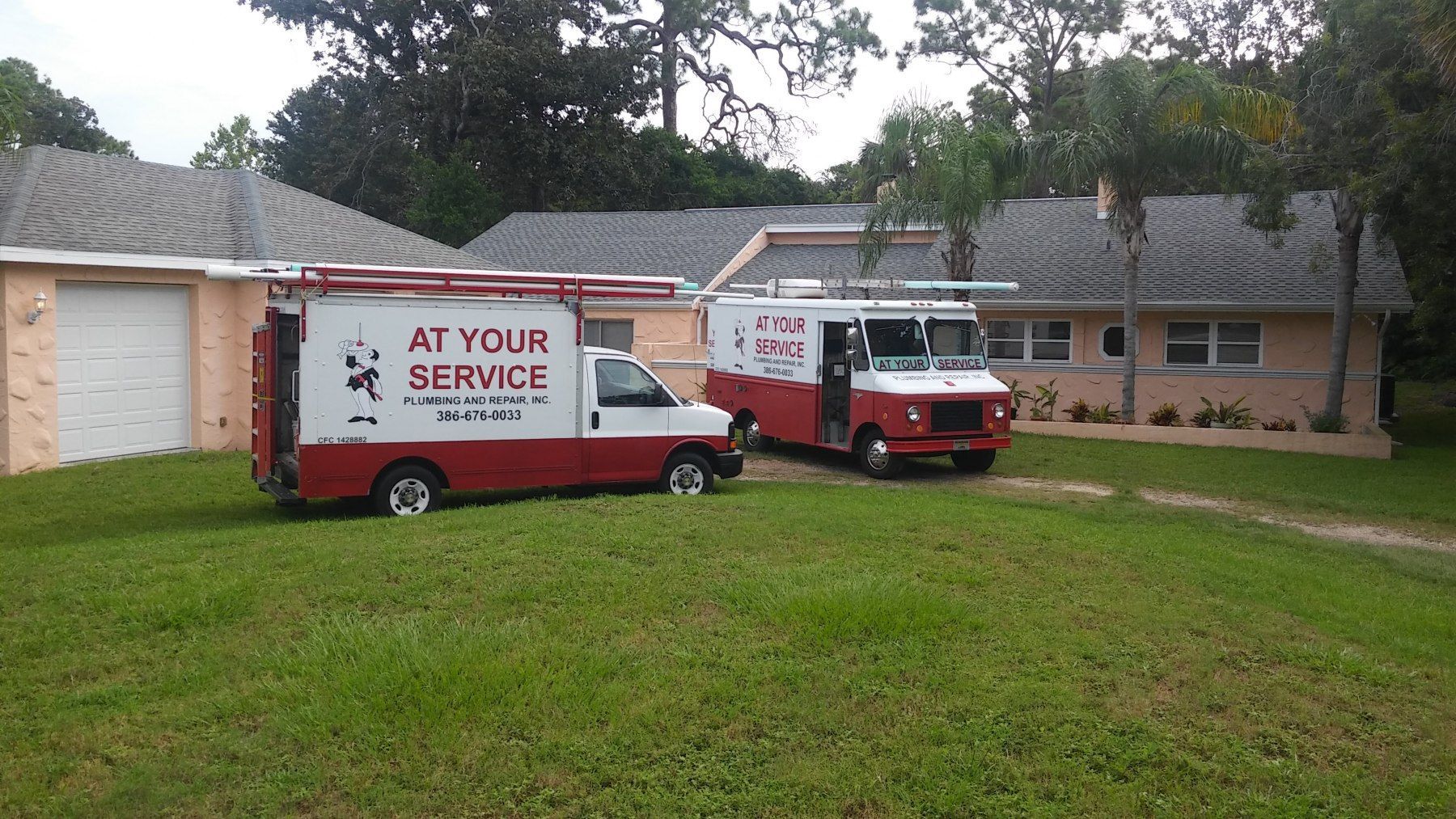 Two red and white service vans parked on a lawn in front of a house.
