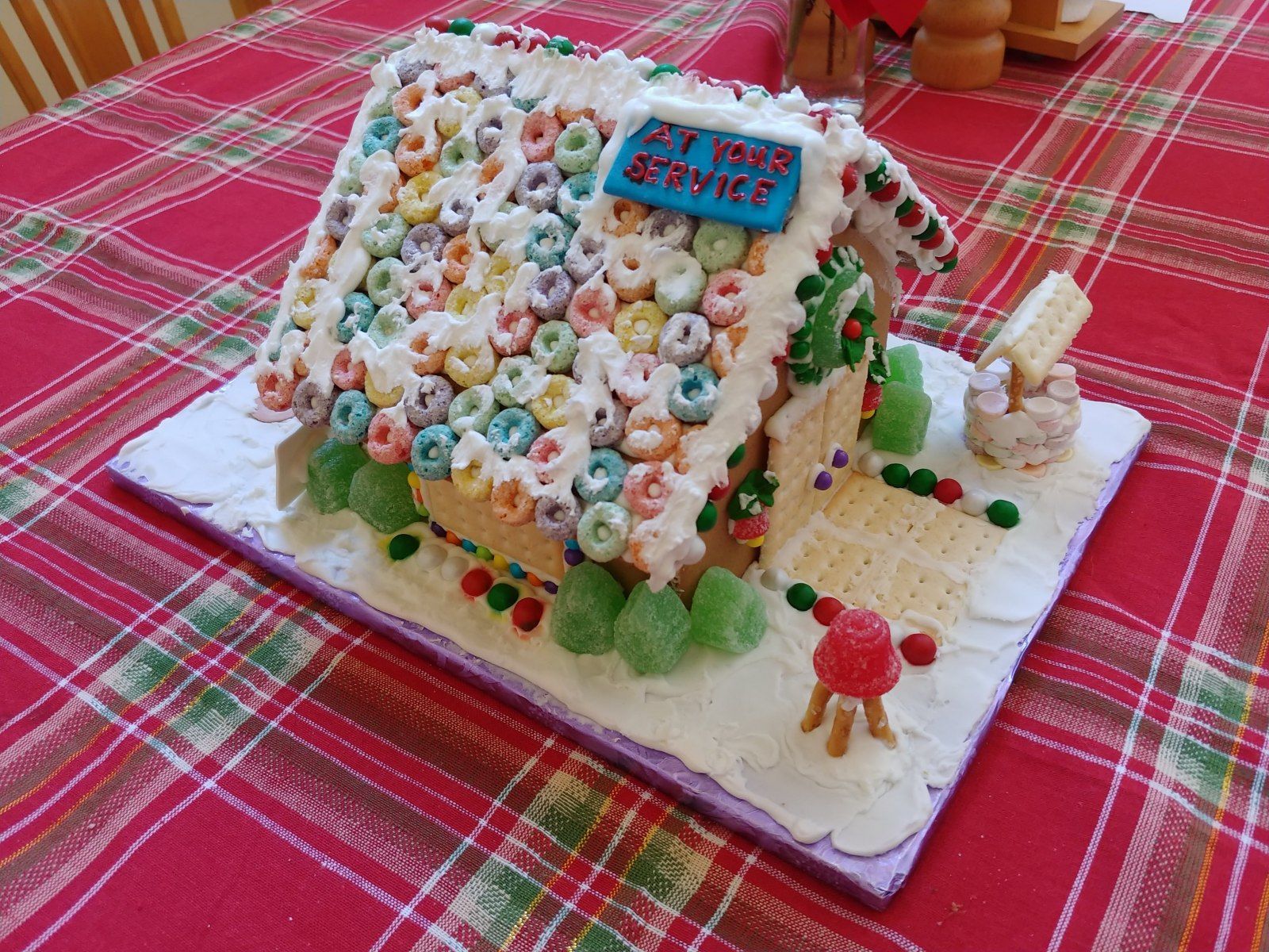 Gingerbread house decorated with colorful cereal, candy, and icing on a white base.
