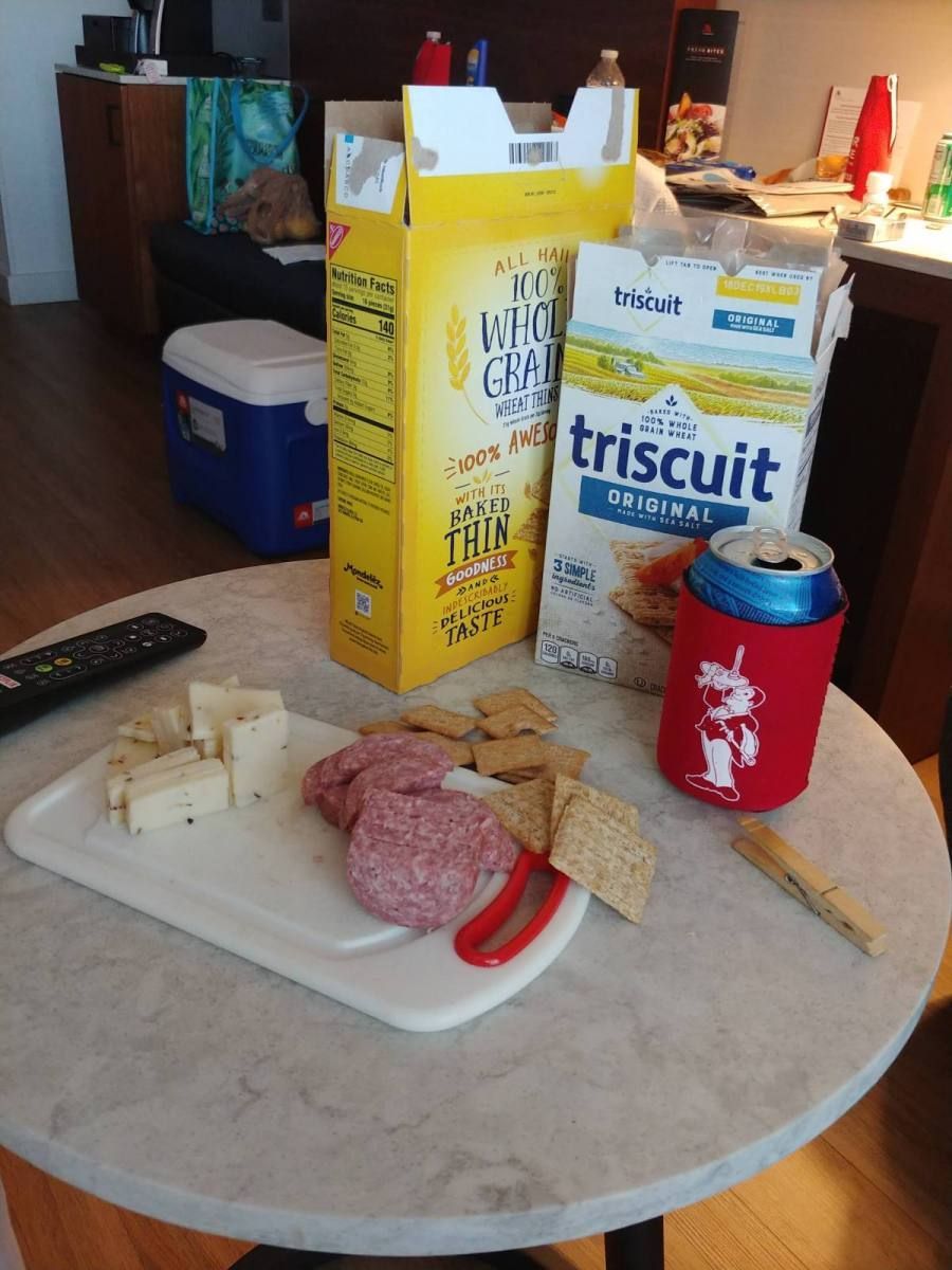 A small table with a cheese and cracker snack plate, boxes of Triscuits and Wheat Thins, and a canned drink.