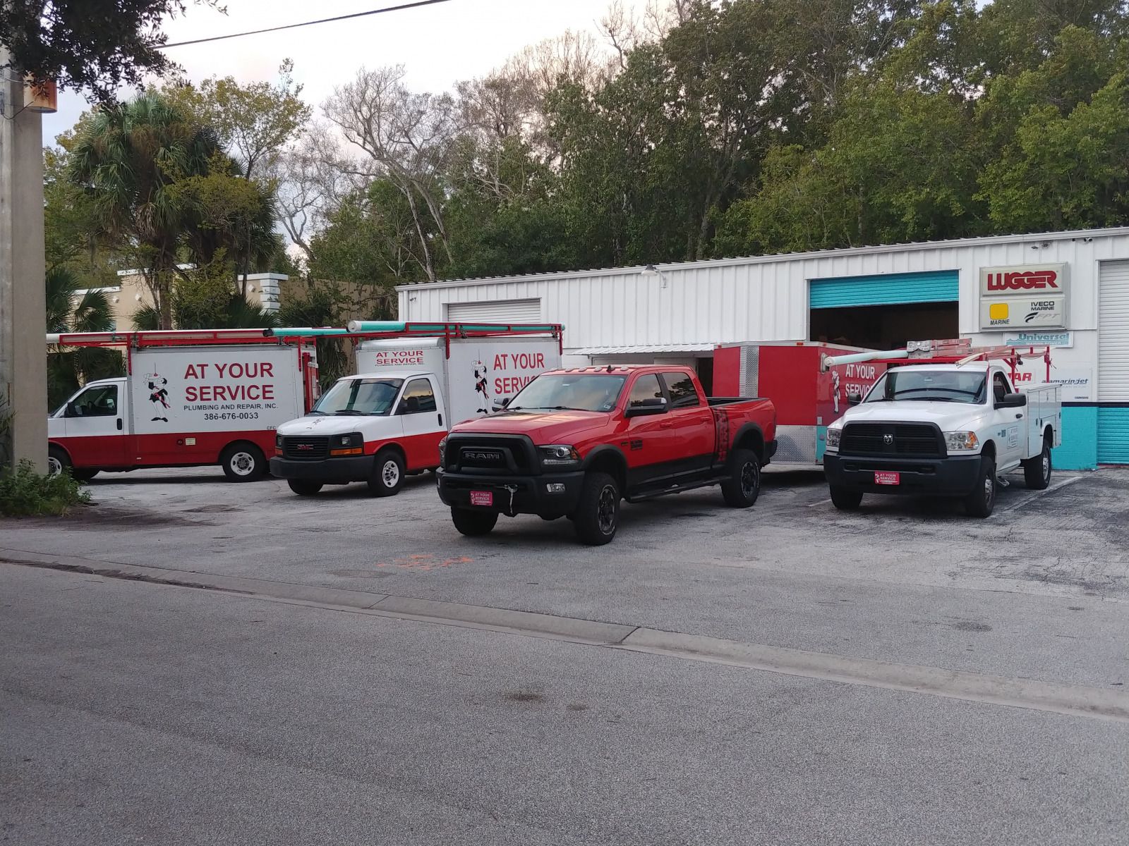 Vehicles parked in front of a white building with open blue doors. Trucks are red and white.