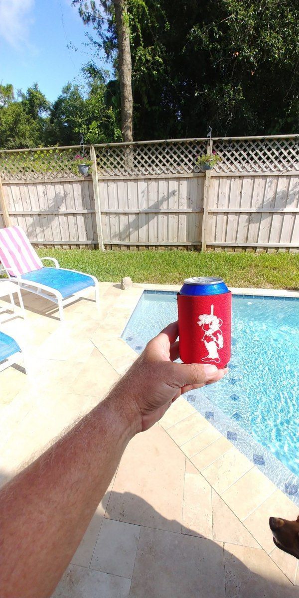 Person holding a red and blue can near a pool on a sunny day.