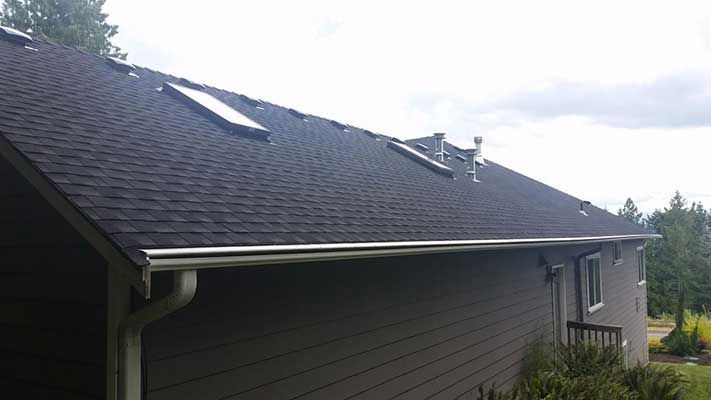A house with a black roof and a skylight on the roof taken by Riverside Roofing