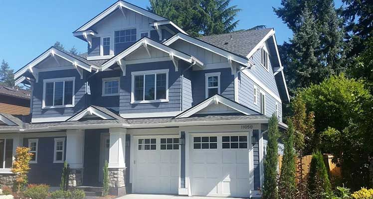 A large house with a white garage door is surrounded by trees on a sunny day taken by Riverside Roofing