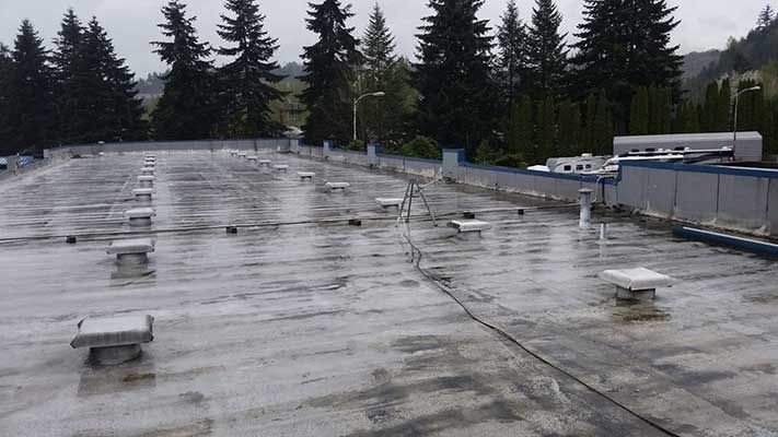 A commercial roof with a lot of vents on it and trees in the background taken by Riverside Roofing