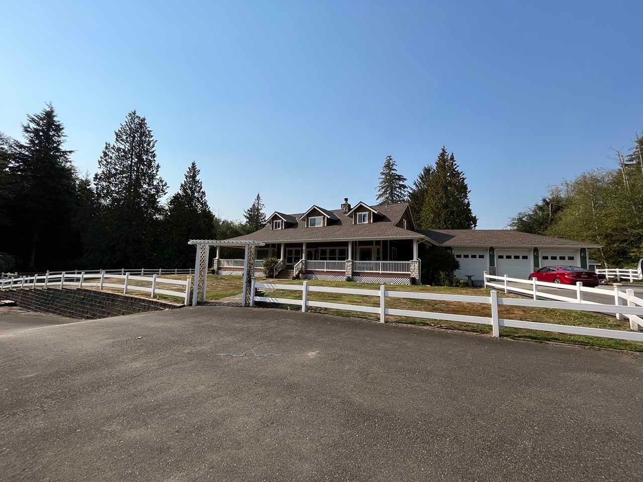 A large house with a white fence around it and a red car parked in front of it taken by Riverside Roofing