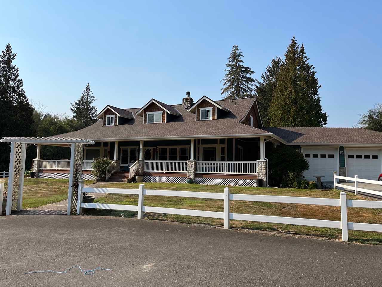 A large house with a porch and a white fence taken by Riverside Roofing