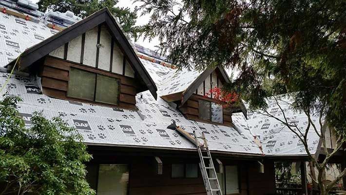 A man is standing on a ladder on the roof of a house taken by Riverside Roofing
