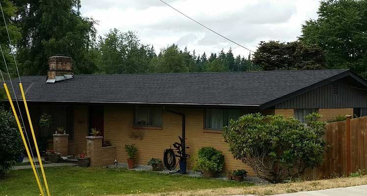 A brick house with a black roof and a fence in front of it taken by Riverside Roofing