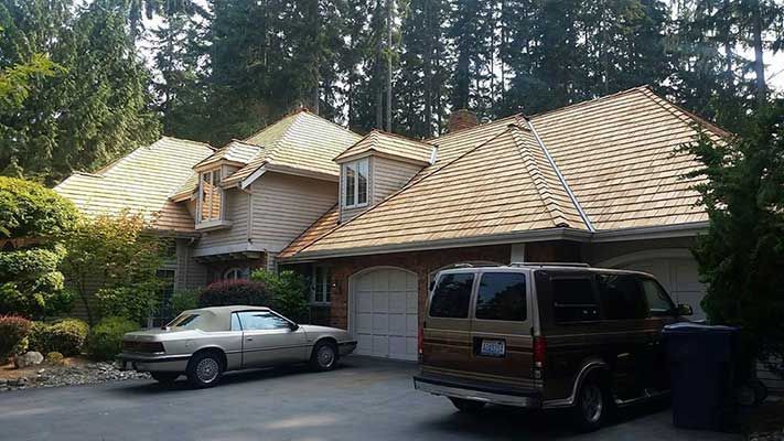 Two cars are parked in front of a large house with a wooden roof taken by Riverside Roofing