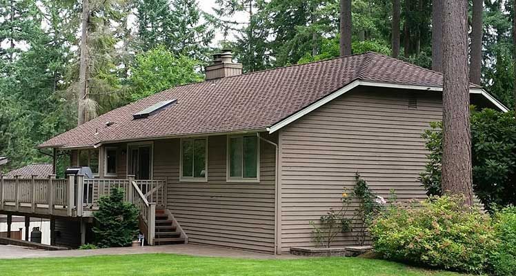 A house with a brown roof is surrounded by trees taken by Riverside Roofing