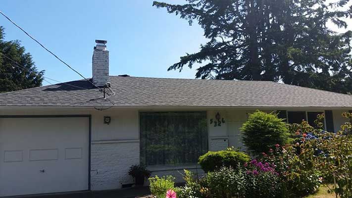 A white house with a gray roof and a chimney taken by Riverside Roofing