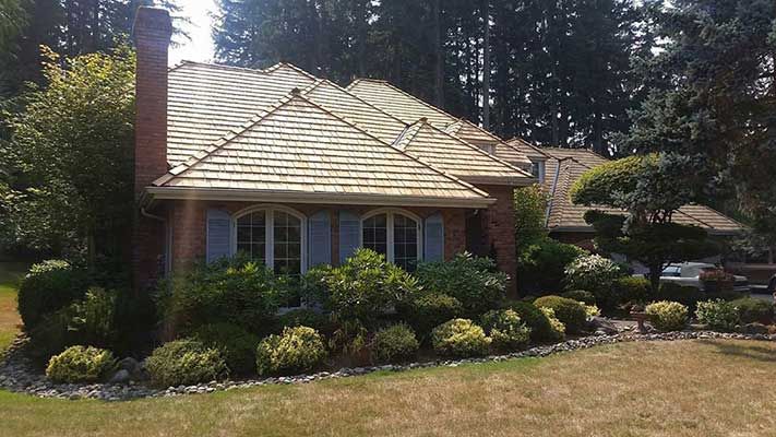 A brick house with a wooden roof and blue shutters taken by Riverside Roofing