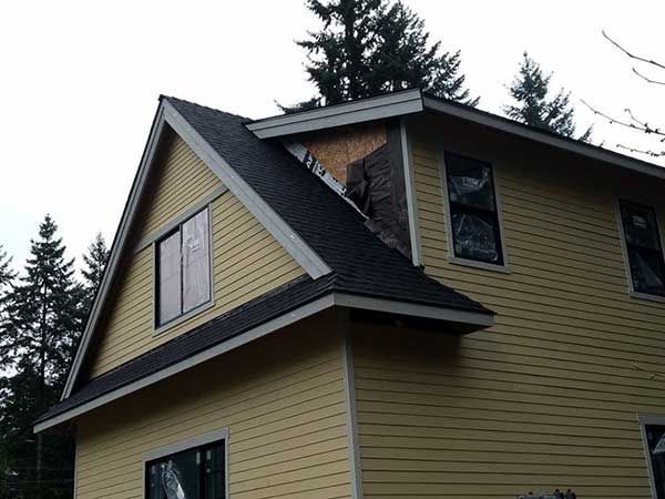 A yellow house with a black roof and trees in the background taken  by local roofer, Riverside Roofing in Marysville WA