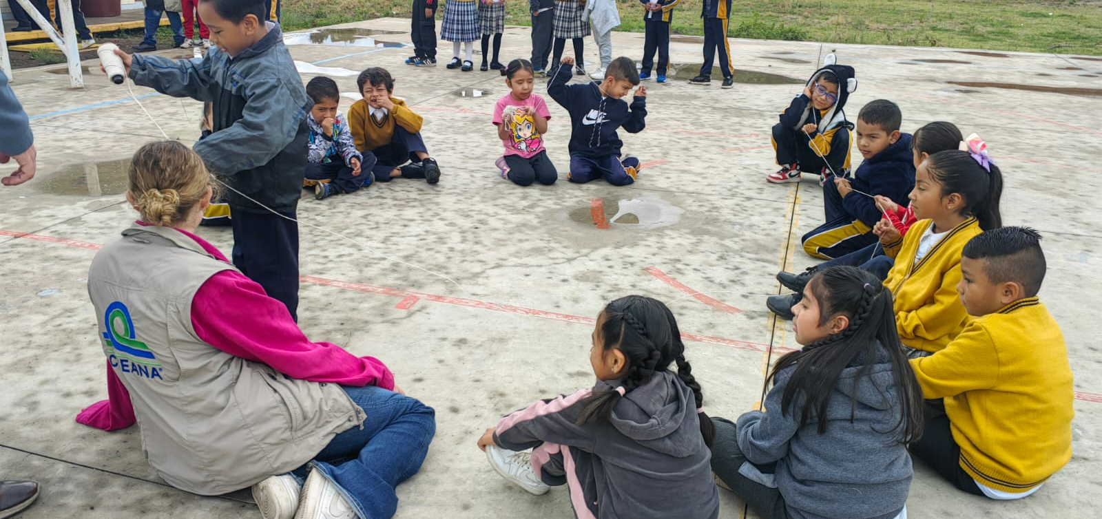 Los niños se sientan en círculo al aire libre mientras un adulto les habla.