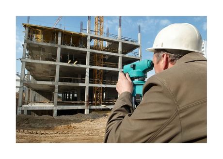 Surveyor wearing a hard hat measuring concrete commercial building