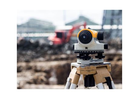 surveying tripod in foreground and excavator in background