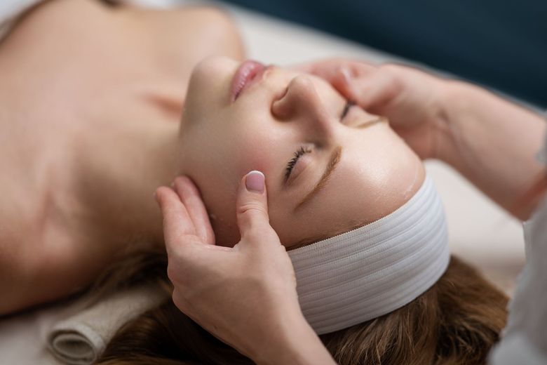 Person receiving a facial massage with a white headband, eyes closed in a spa setting