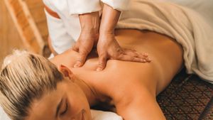 Massage therapist kneading a client’s back on a spa table, with a beige towel nearby