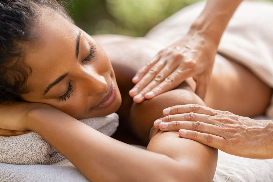 A person with closed eyes receiving a relaxing massage on their shoulder and upper arm while lying on a soft towel.